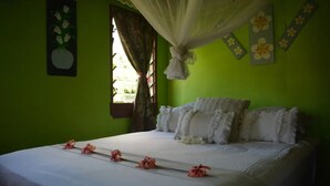 Ein Bett mit weißen Leinen und rosa Blumen, eine grüne Wand und ein Fenster mit Vorhängen.