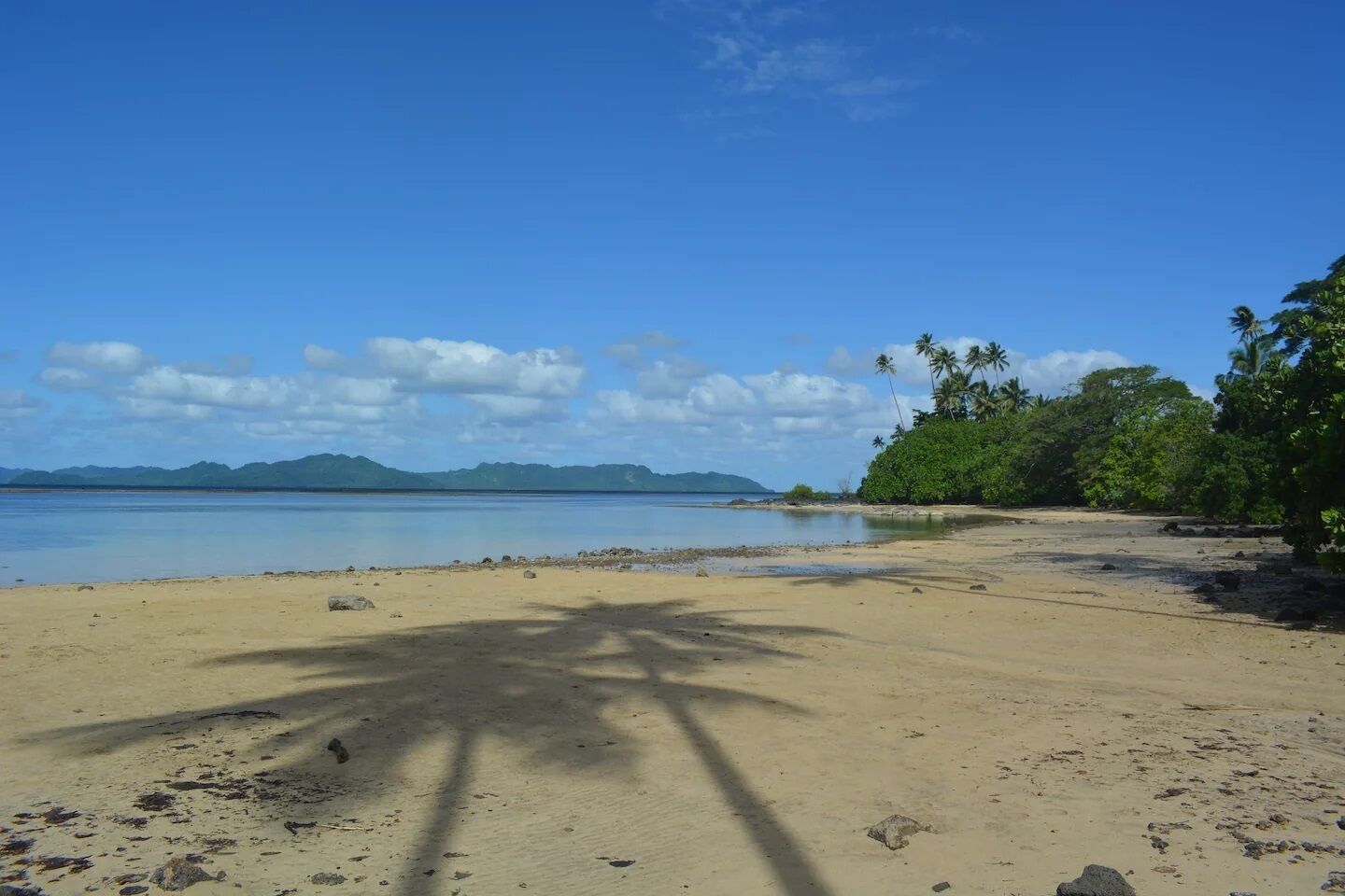 A beach with clear skies, calm water, and distant mountains.
