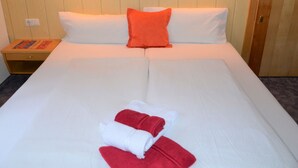 Ein ordentlich bezogenes Bett mit weißer und roter Bettwäsche, ein hölzerner Kopfteil und ein Nachttisch mit einem Buch und einer Lampe.