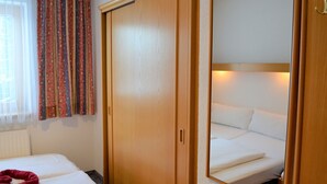 Une chambre d’hôtel avec un lit, une armoire, un miroir et une fenêtre avec des rideaux.