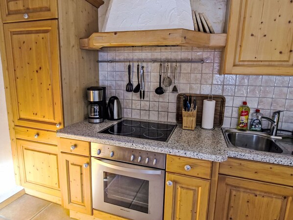 Une cuisine avec des meubles de rangement en bois, une cuisinière en acier inoxydable, une machine à café et divers ustensiles accrochés au mur.