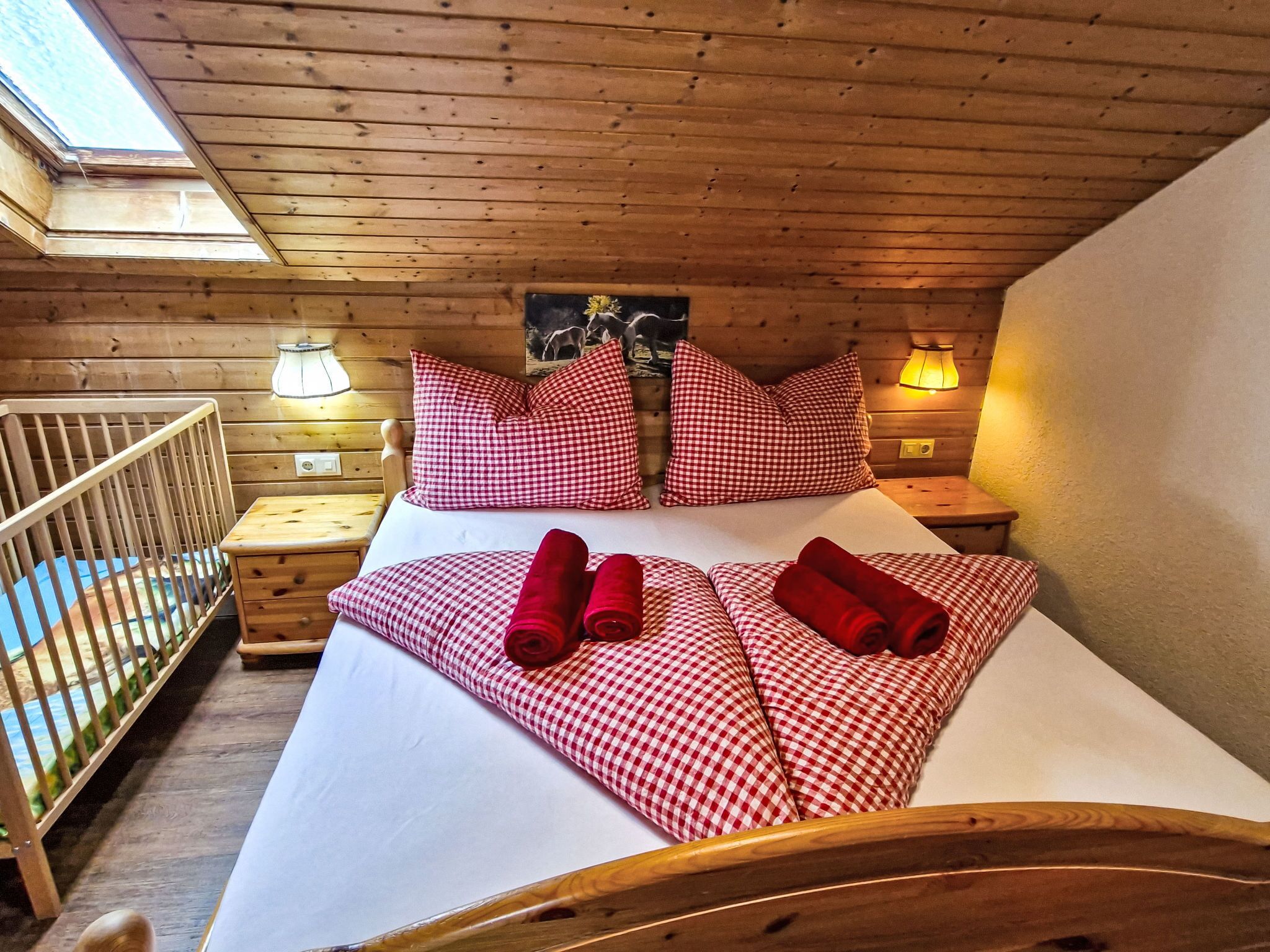 Una habitación tipo cabaña de madera con una cama, almohadones a cuadros, una mesita de noche y una lámpara.