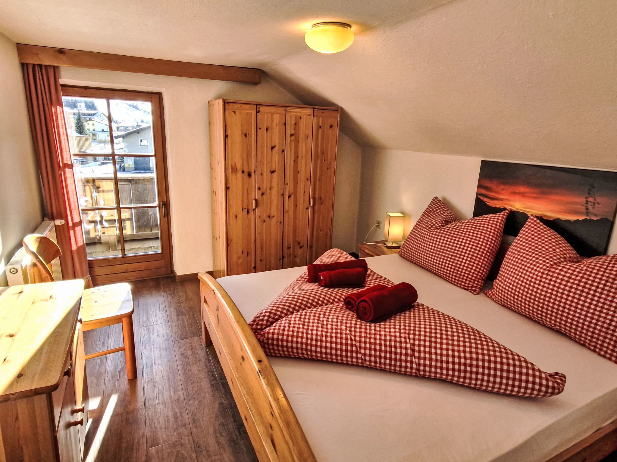 Une chambre confortable avec un lit en bois, des coussins à carreaux, une armoire en bois et une vue sur l’extérieur par une fenêtre.