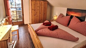 A cozy bedroom with a wooden bed, checkered pillows, a wooden wardrobe, and a view of the outside through a window.