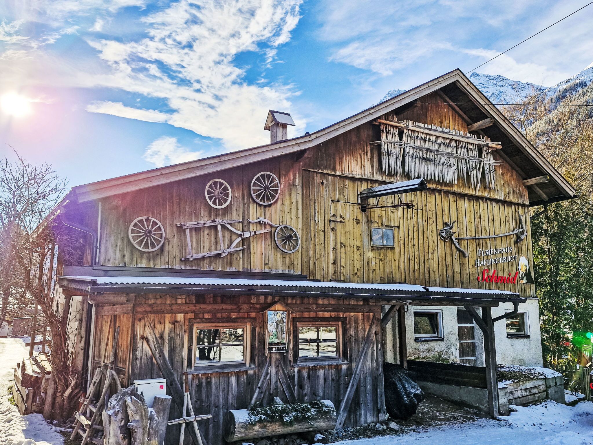 A wooden building with a sloped roof, large windows, and a sign that reads "FERIENHAUS HAFINGERJOF".