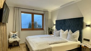 A bedroom with a large bed, a window with curtains, a chair, and a bedside table. - Panorama Chalet Tirol by Interhome (Auffach)
