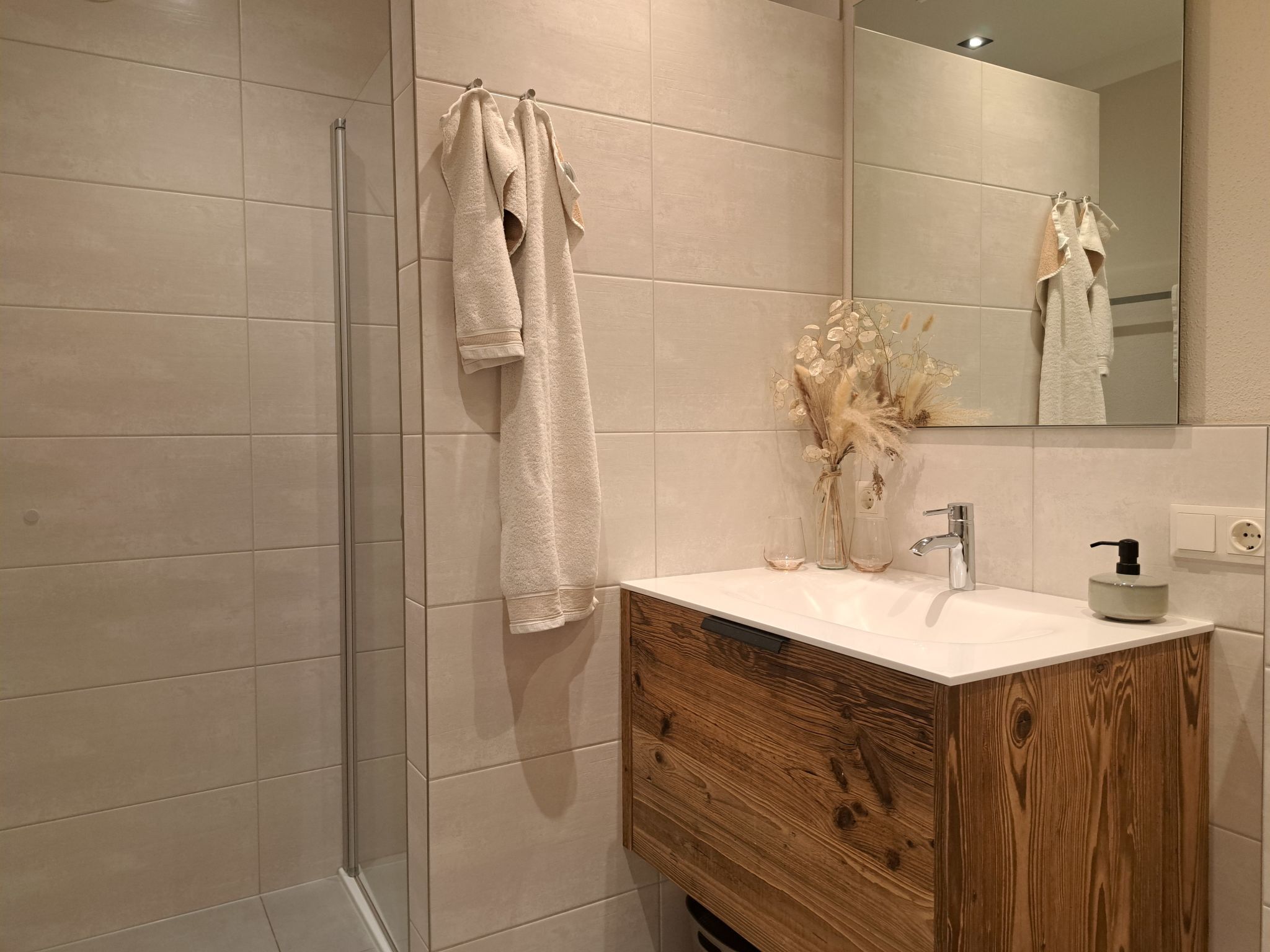 Une salle de bain moderne avec une douche à parois de verre, un meuble-lavabo en bois et un miroir.