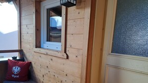 Una cabaña de madera con ventana, un banco y un cojín con un escudo.