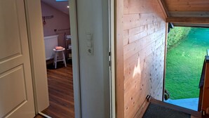 Pared exterior de madera con una puerta que da a una habitación con un radiador, un taburete pequeño y una decoración con forma de corazón.