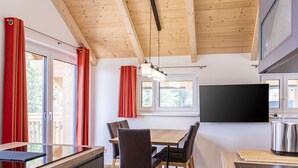 A modern kitchen with wooden beams, a dining area with a table and chairs, and a large window with red curtains. - für bis zu 8 Personen + Hot Tub by Interhome (Turracher Höhe)