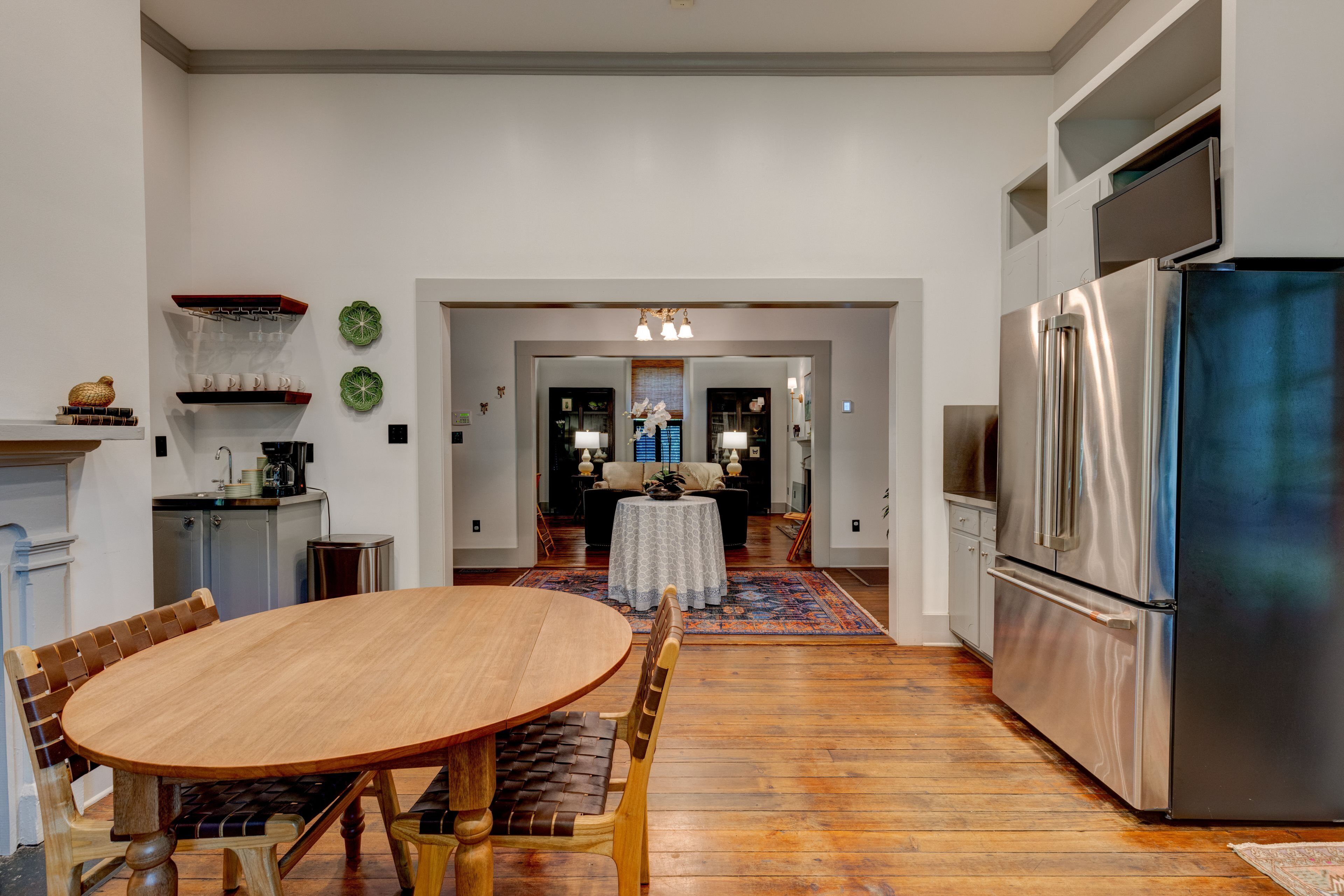 A modern kitchen with a stainless steel refrigerator, wooden dining table, and chairs. There is a small island with a sink and a countertop.