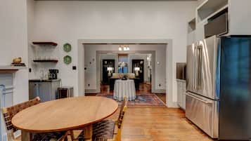 A modern kitchen with a stainless steel refrigerator, wooden dining table, and chairs. There is a small island with a sink and a countertop.
