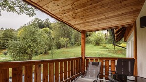 Un terrazzo in legno con ringhiera in vetro che si affaccia su un'area verde alberata.