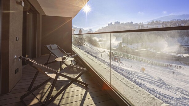 A balcony with sun lounger chairs, a glass railing, and a view of a snowy landscape with buildings and trees. - mit 1 Schlafzimmer für 2-4 Personen by Interhome (Hopfgarten im Brixental)