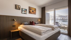A modern bedroom with a large bed, a bedside table, a bench, and a view of a snowy landscape through a large window. - mit 1 Schlafzimmer für 2-4 Personen by Interhome (Hopfgarten im Brixental)
