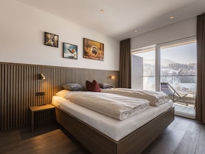 A modern bedroom with a large bed, a bedside table, a bench, and a view of a snowy landscape through a large window.