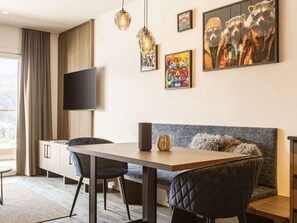 Een moderne eetruimte met een houten tafel, zwarte stoelen, een grijze bank en een flatscreen televisie aan de muur.