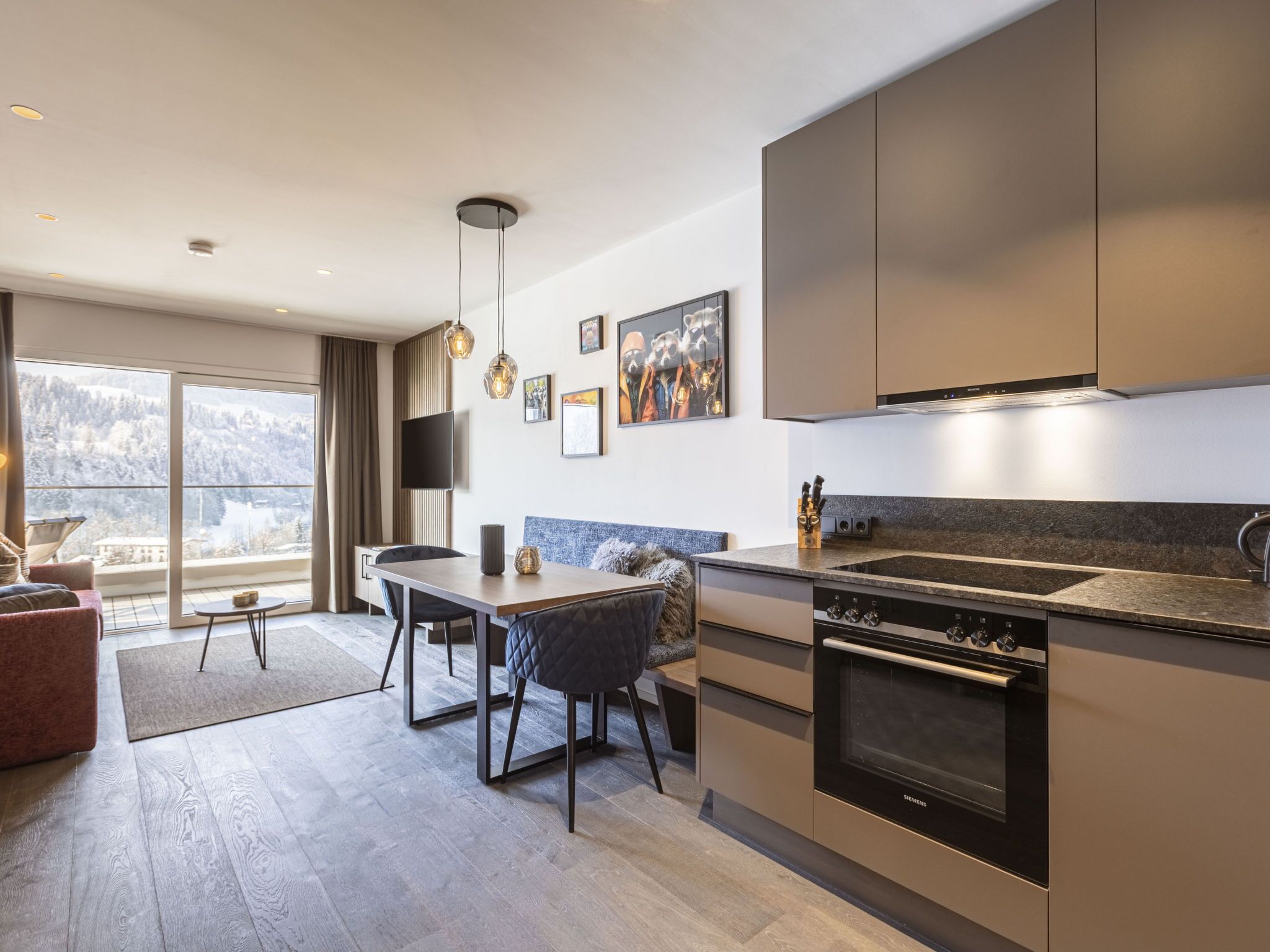 Eine moderne Küche mit Einbauofen, ein Essbereich mit Tisch und Stühlen sowie ein großes Fenster mit Blick ins Freie.