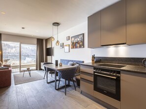Een moderne keuken met een ingebouwde oven, een eethoek met een tafel en stoelen, en een groot raam met uitzicht op de omgeving.