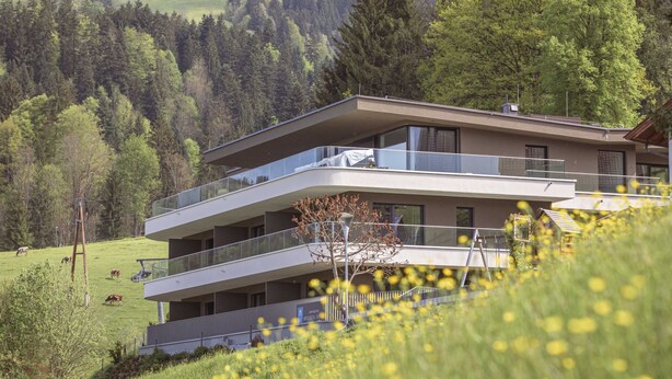 Ein modernes Mehrgeschosshaus mit Balkonen, umgeben von üppiger, grüner Landschaft und einem Tal.