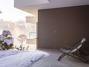 En modern inredning med ett trädäck, en solstol och utsikt över snöklädda träd.