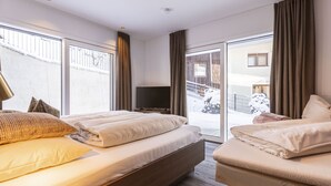 Ein Hotelzimmer mit einem großen Bett, einem Fernseher und einer Glasschiebetür zu einem verschneiten Außenbereich.