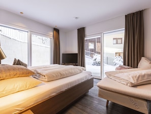 Ett hotellrum med en stor säng, en tv och en skjutdörr i glas som leder ut till ett snötäckt område.