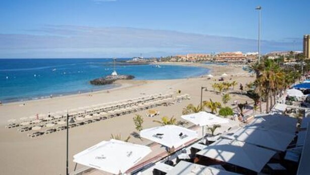 A beachside hotel with rows of sunbeds and umbrellas, a clear view of the ocean, and a distant view of the city. - Home2Book Calm Ocean Los Cristianos (Los Cristianos)