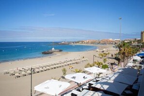 Un hotel sulla spiaggia con file di lettini e ombrelloni, una vista limpida sull'oceano e una prospettiva lontana sulla città.