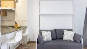 A modern kitchen with white bar stools, a grey sofa with patterned cushions, and a white cabinet above the counter. - Home2Book Calm Ocean Los Cristianos (Los Cristianos)