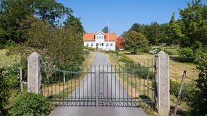 Portilla varustettu sisäänkäynti kiinteistöön, jonne johtaa asfaltoitu ajotie. Ajotie päättyy valkoiseen rakennukseen, jonka katto on punainen.