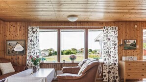A cozy room with wooden walls and ceiling, a brown leather sofa, a table with a white tablecloth, and a view of greenery outside.
