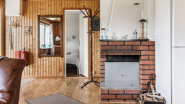 A cozy room with wooden walls, a brick fireplace, a bed, and a door leading to another room.