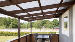 A covered outdoor seating area with a wooden table and chairs, overlooking a fenced field.