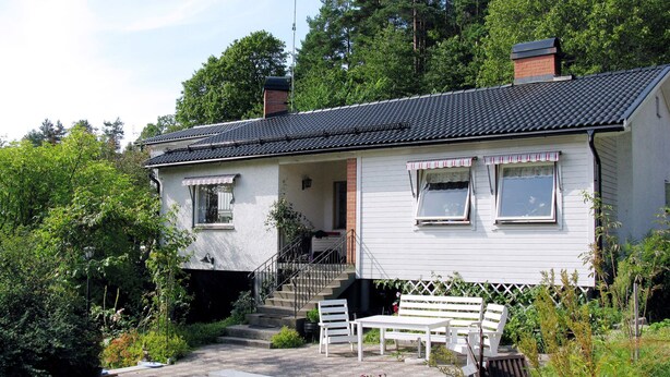 Ein zweistöckiges Haus mit Veranda, Schornstein und Satellitenschüssel.