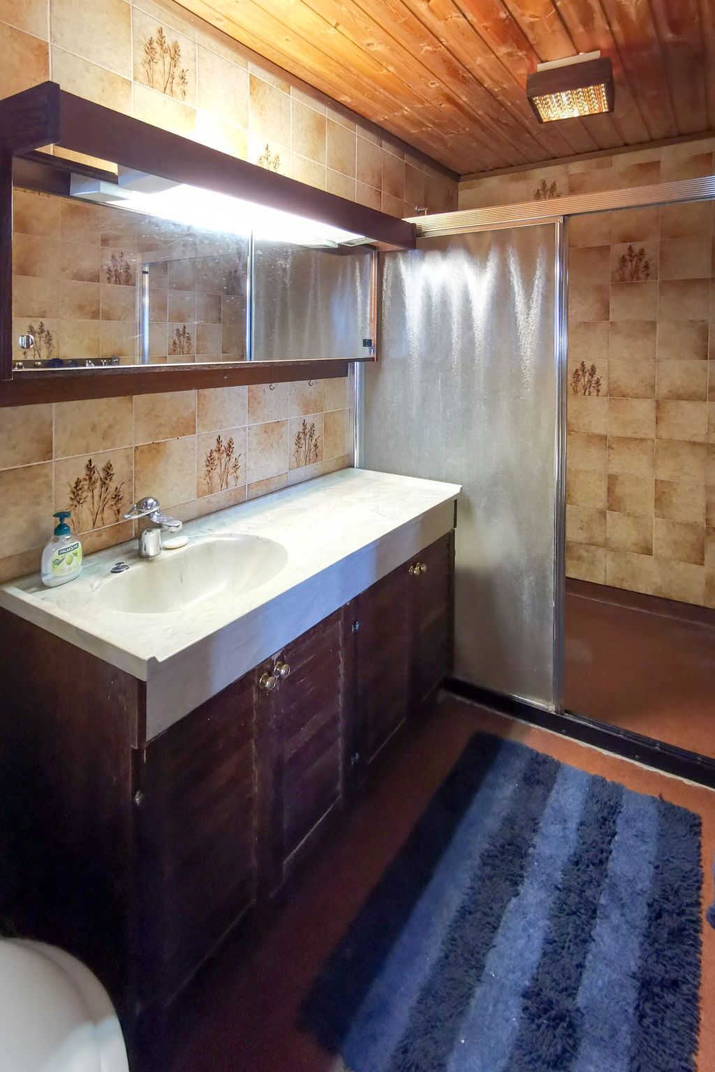 A bathroom with a wooden ceiling, a white sink, dark wooden cabinets, a mirror, and a shower curtain.
