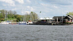 Zona costera con barcos amarrados, una bandera y un edificio con porche.