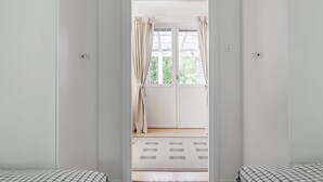 A room with two beds, a door leading to a balcony, and a view of greenery outside. - Lindby Pärlan by Interhome (Adelsö)