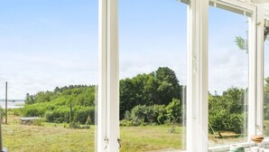 A room with a large window overlooking a grassy area with trees and a body of water. - Lindby Pärlan by Interhome (Adelsö)
