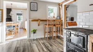 A kitchen with a wooden table, chairs, a stove, and a hanging light fixture. - Aspenäs by Interhome (Sandhem)