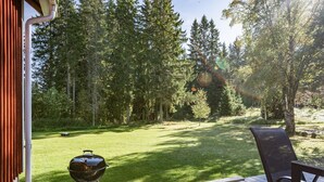 A wooden deck with a grill and a chair, overlooking a grassy yard with trees. - Aspenäs by Interhome (Sandhem)