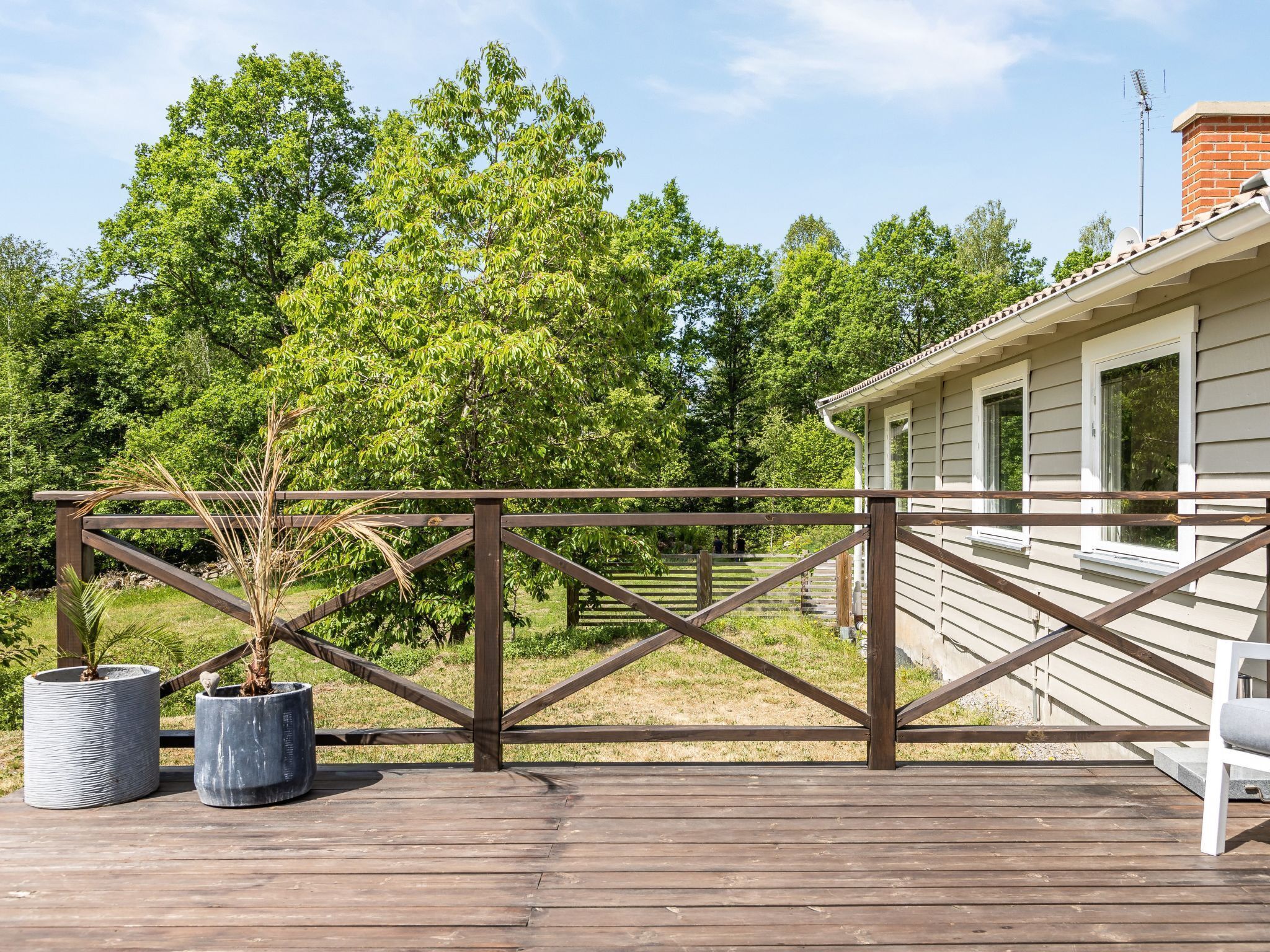 A wooden deck with a metal gate, potted plants, and a house in the background.
