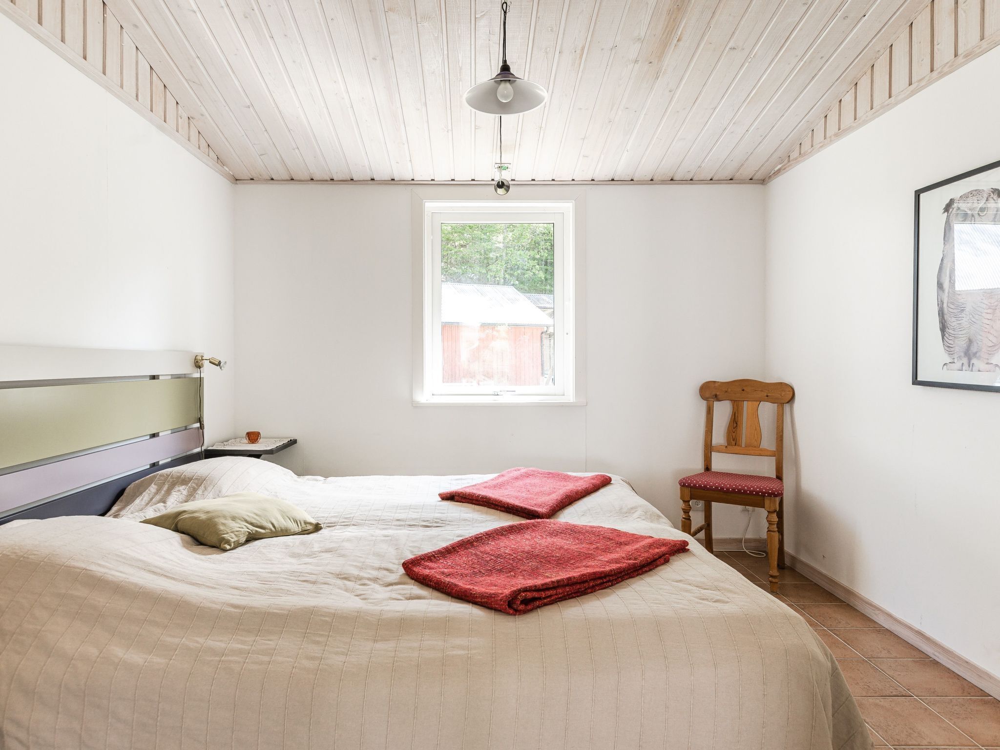 Une chambre à coucher avec un lit, une chaise en bois, une fenêtre et un luminaire suspendu.