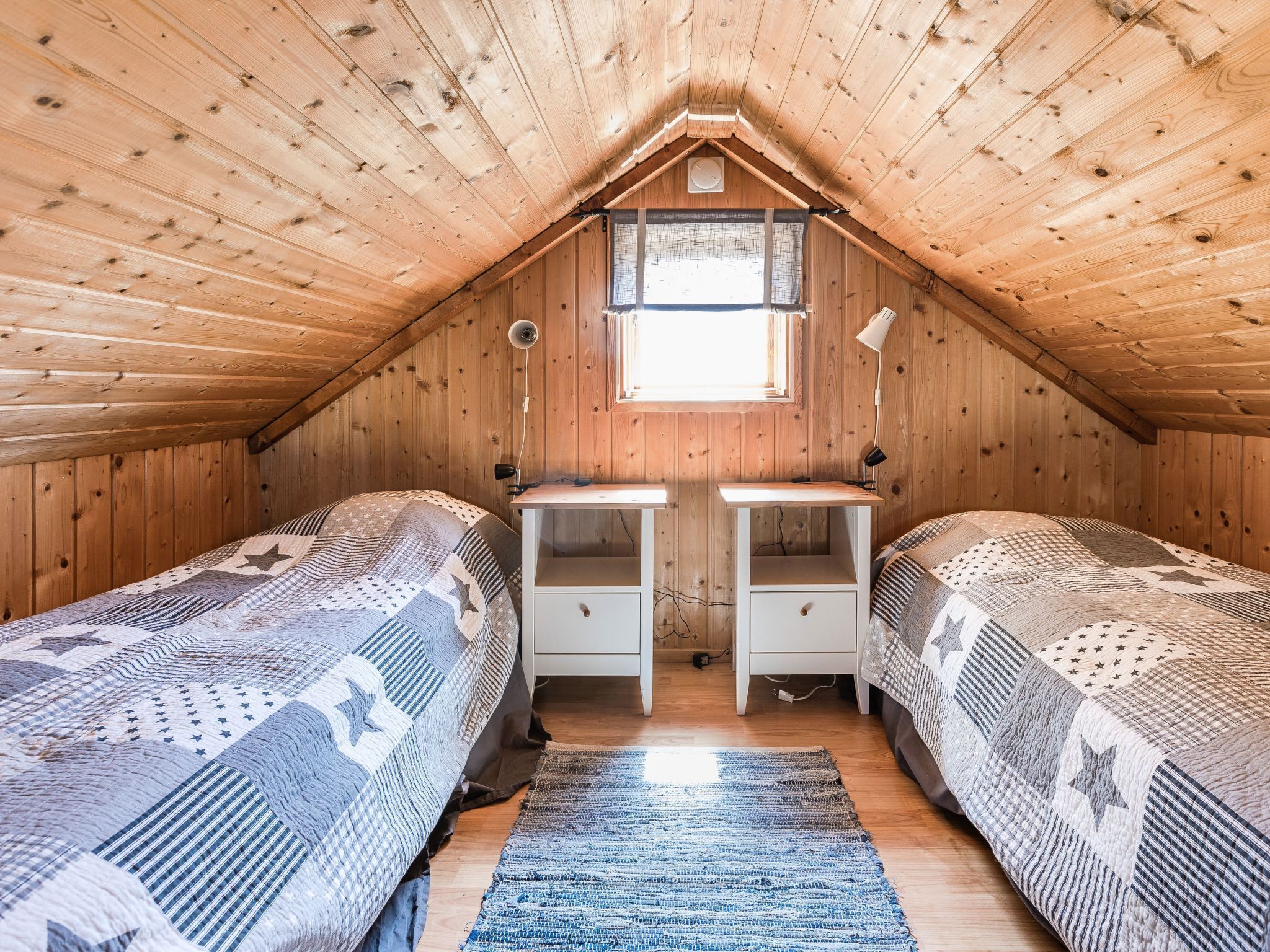 A cozy attic bedroom with two beds, a small window, and a desk.