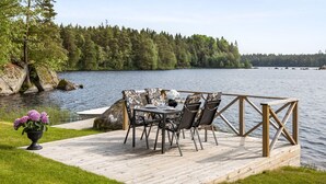 Une terrasse en bois avec une table et des chaises, donnant sur un lac et entourée d’arbres.