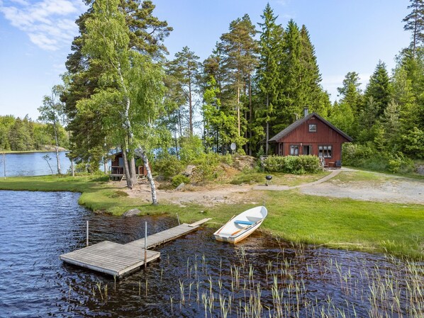 A lakeside cabin with a dock, surrounded by dense forest and a clear sky.