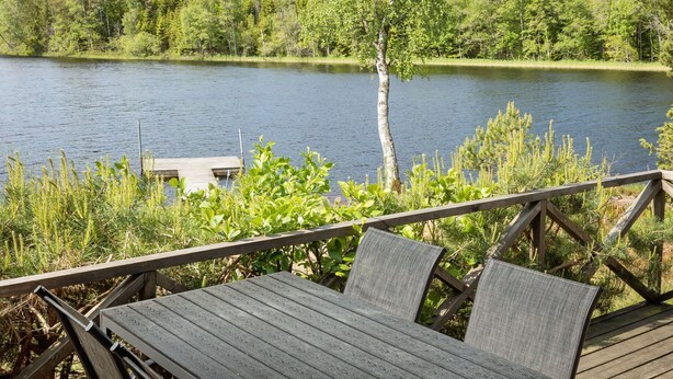 A wooden deck with a table and chairs overlooking a lake, surrounded by dense forest. - Kasen Sjökanten by Interhome (Färgelanda)