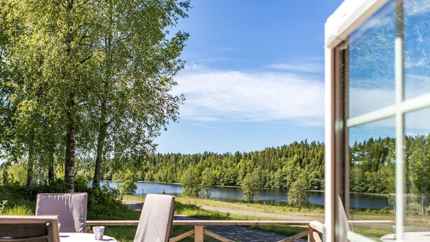 An outdoor deck with a table and chairs, overlooking a lake and forest. - Mjöhult Utsikten by Interhome (Ätran)