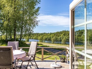 En udendørs terrasse med et bord og stole, med udsigt over en sø og en skov.