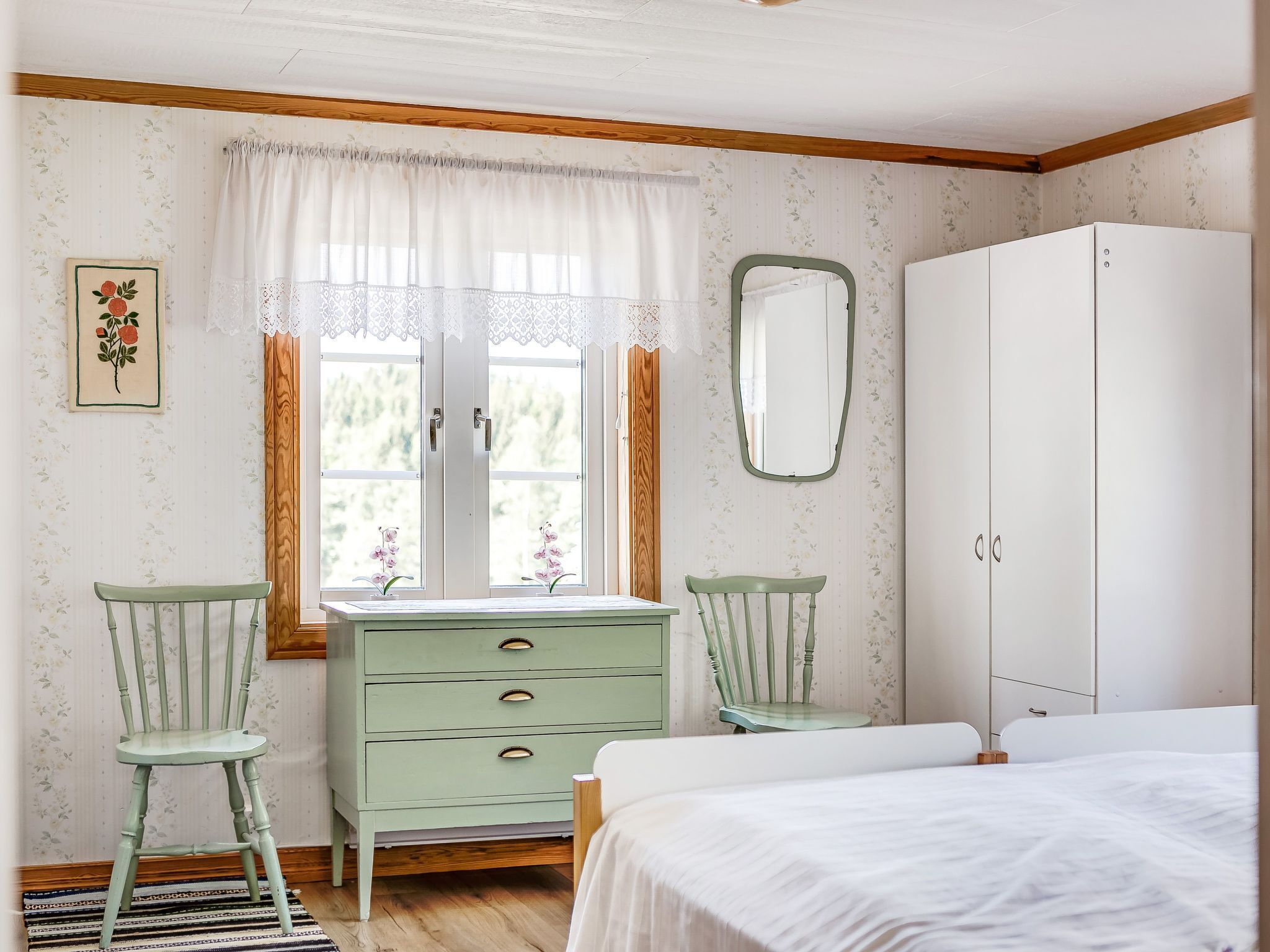 Un dormitorio con cama, cómoda, dos sillas, espejo y ventana con cortinas.